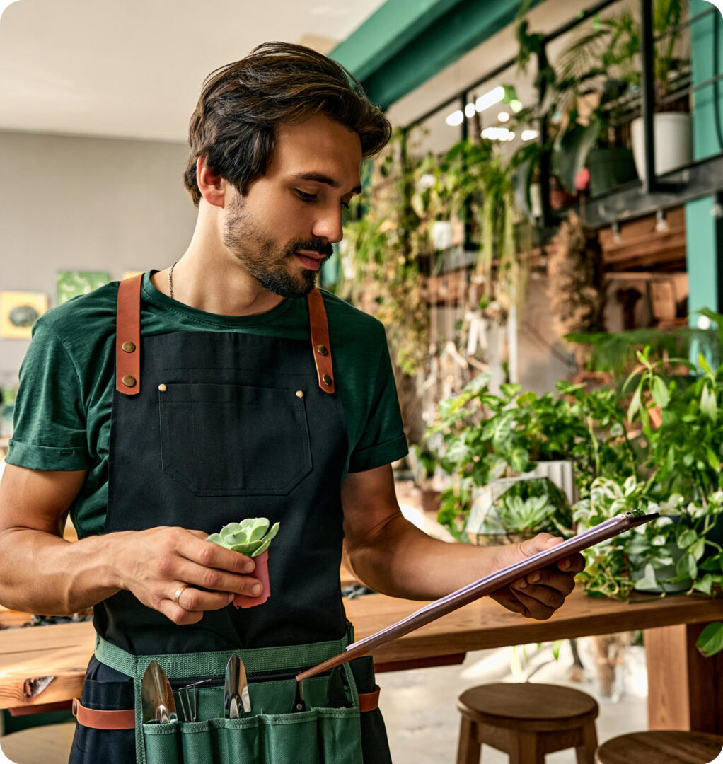 Man in apron holding plant and clipboard.